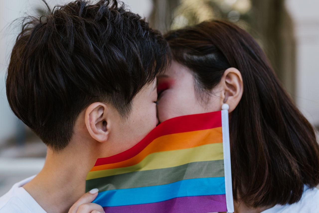 Close-up of a couple kissing behind a pride flag, expressing love and LGBTQ+ pride.