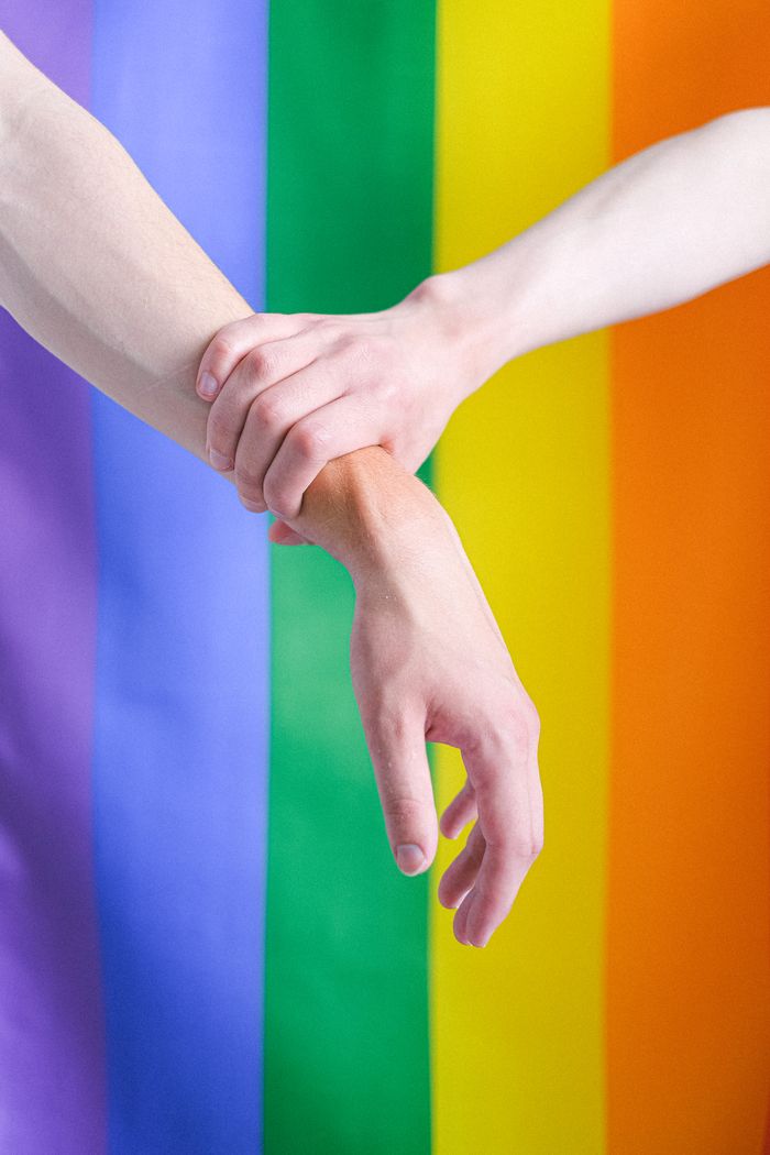 Two hands clasped against a vibrant LGBT pride flag background, representing unity and support.